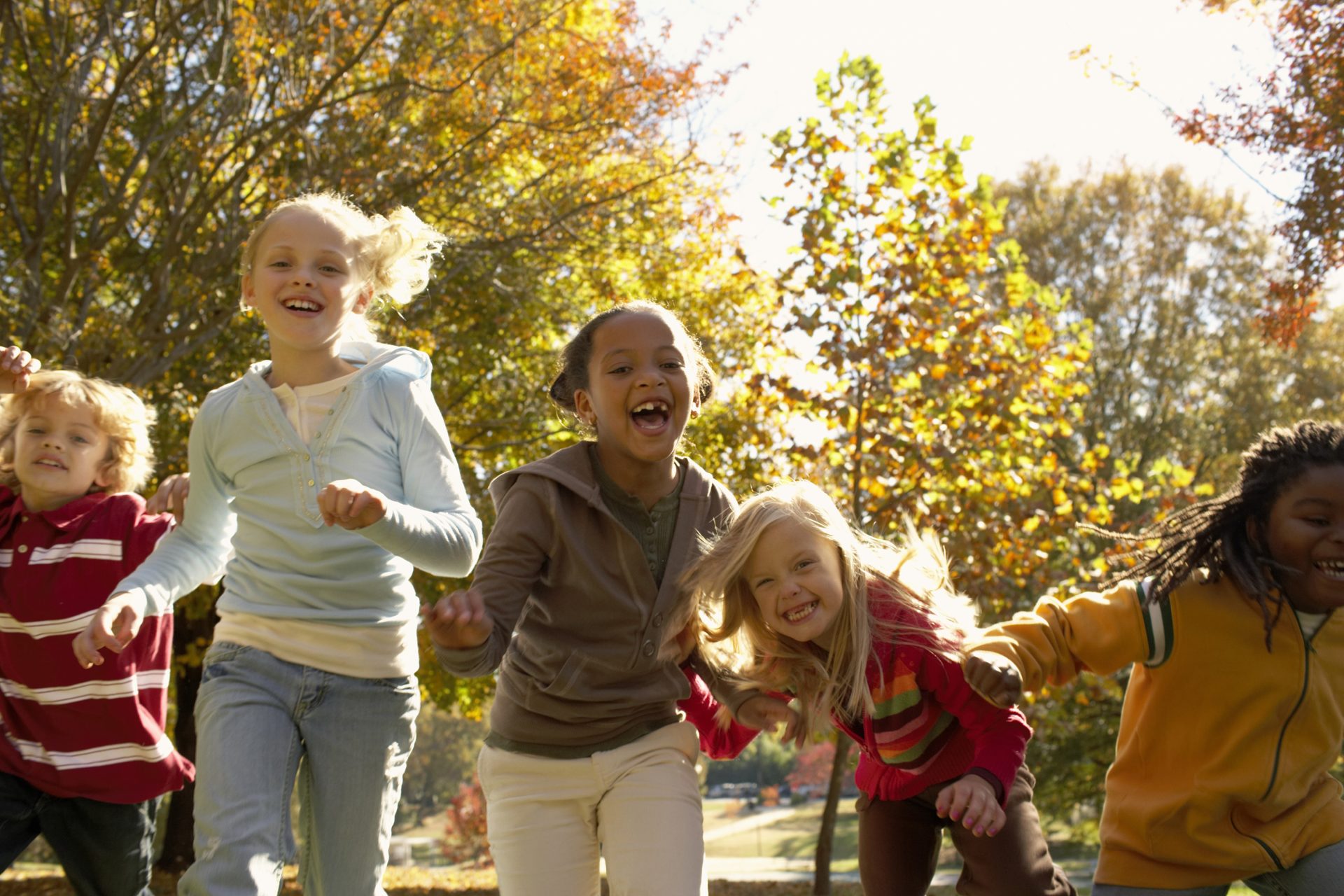 Group of children running and laughing with fall trees in background